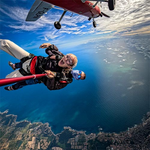 Saut en parachute tandem au-dessus de la côte vendéenne, la passagère exprime sa joie en chute libre tandis que le Cessna blanc et rouge s'éloigne dans un ciel bleu azur teinté des premières lueurs du couchant