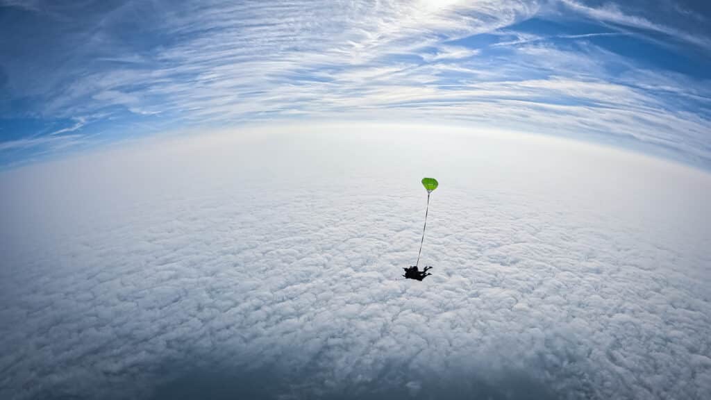 Tandem HALO au-dessus des nuages. La photo a été prise à 6000 mètres de hauteur, on y voit les parachutistes survoler un tapis blanc de cumulus.